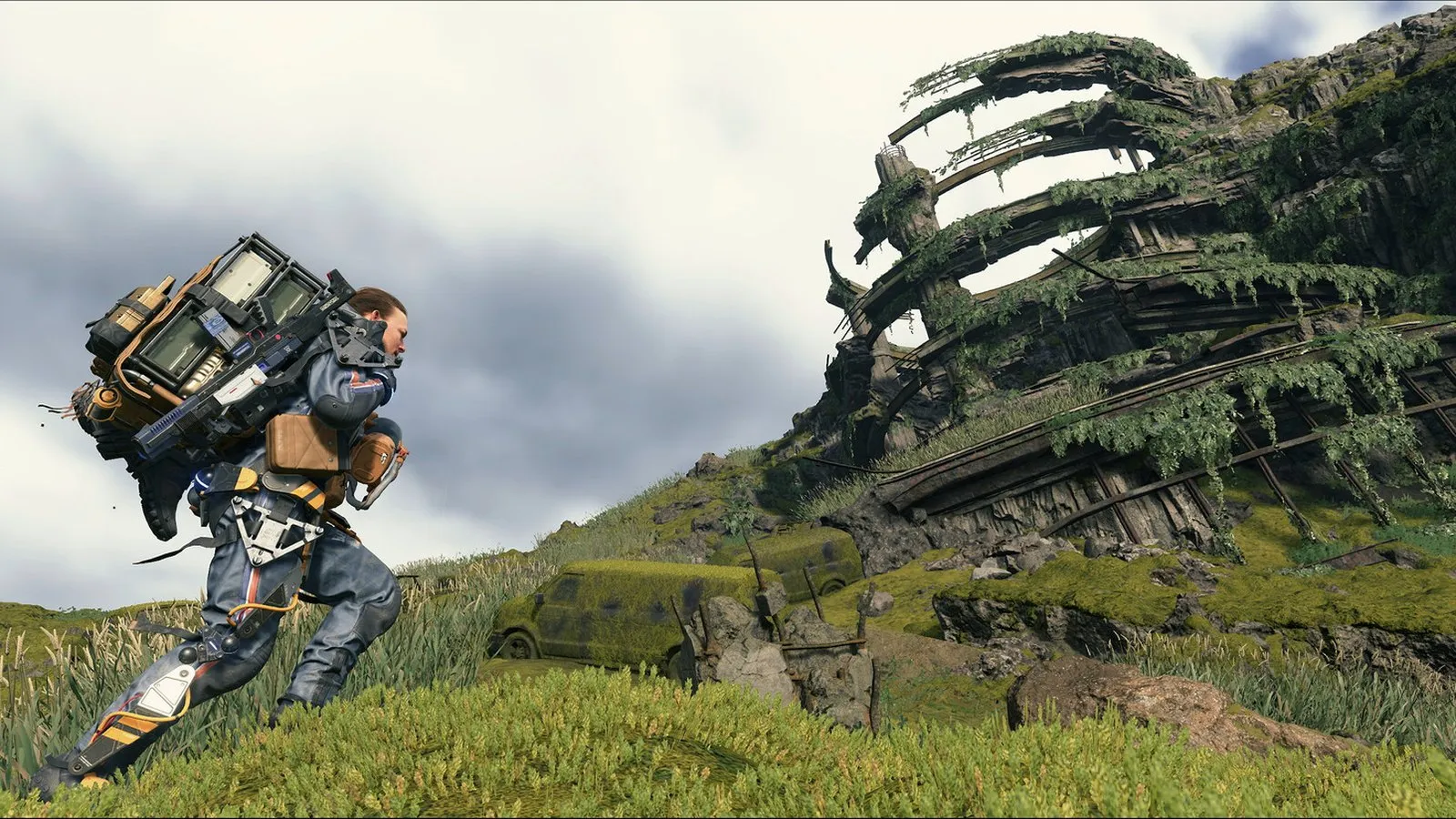 Sam camina cargado de paquetes por una pradera junto a un barco varado cubierto de musgo en Death Stranding Director's Cut