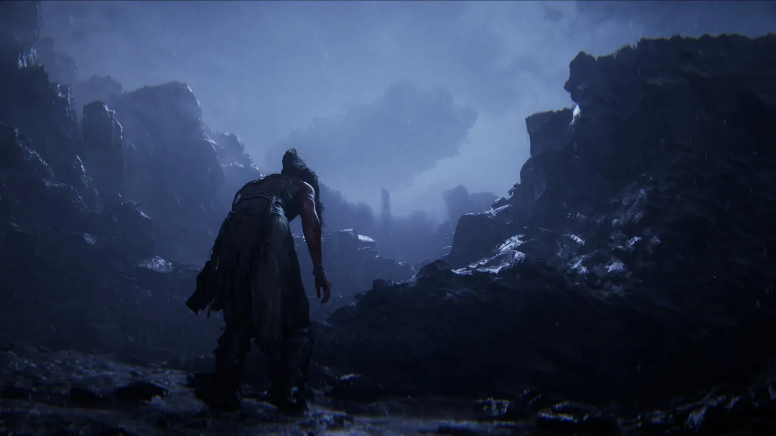 Senua camina por una playa de rocas negras bajo acantilados en Senua's Saga: Hellblade II