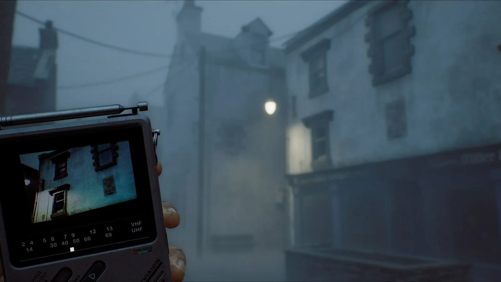 Una mano sostiene un pequeño dispositivo con pantalla en una calle con niebla en SILENT HILL: Townfall