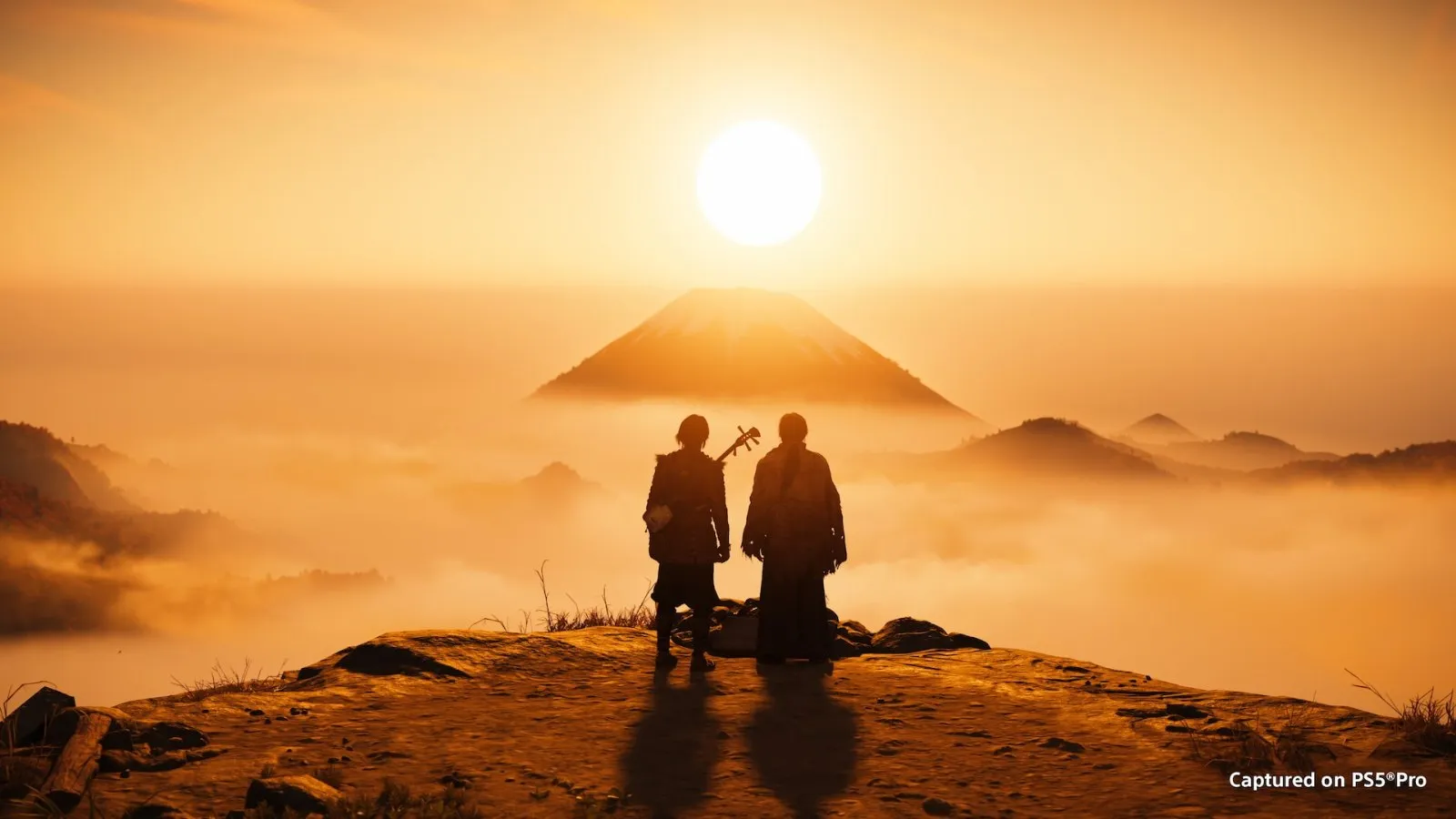 Dos figuras contemplan el atardecer sobre el monte Yōtei en Ghost of Yōtei